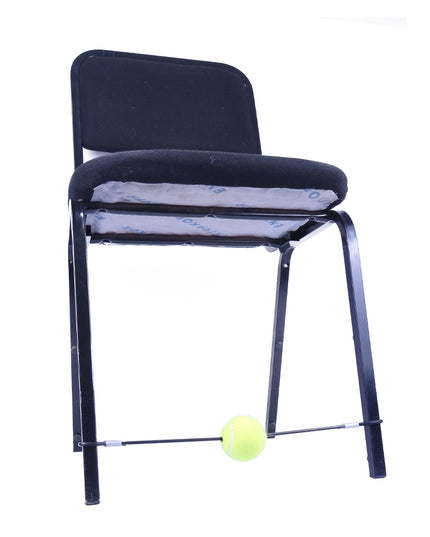 A chair with a black cushion and a rubber band attached to its front two legs, ending in a tennis ball.